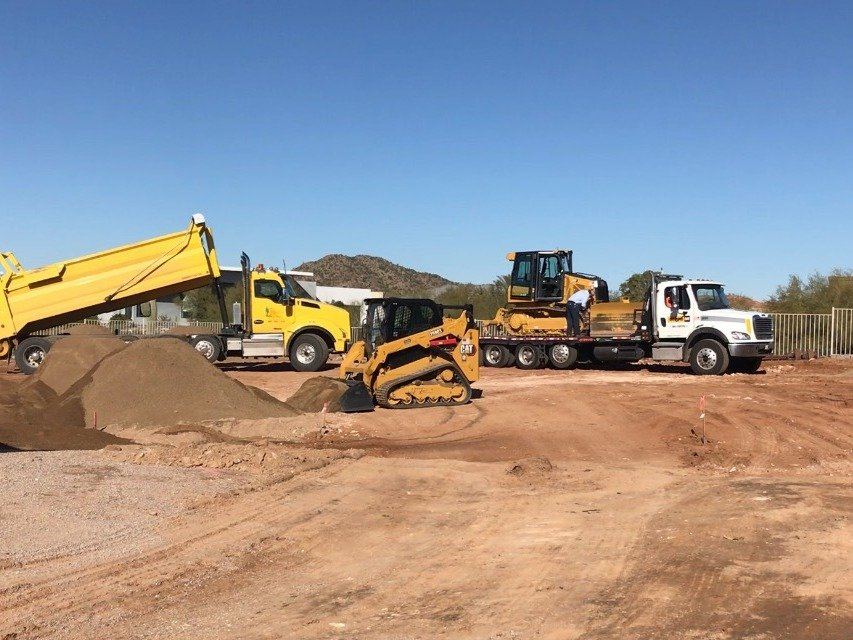 Dump trucks and a trailered dozer moving equipment with mountains in the background