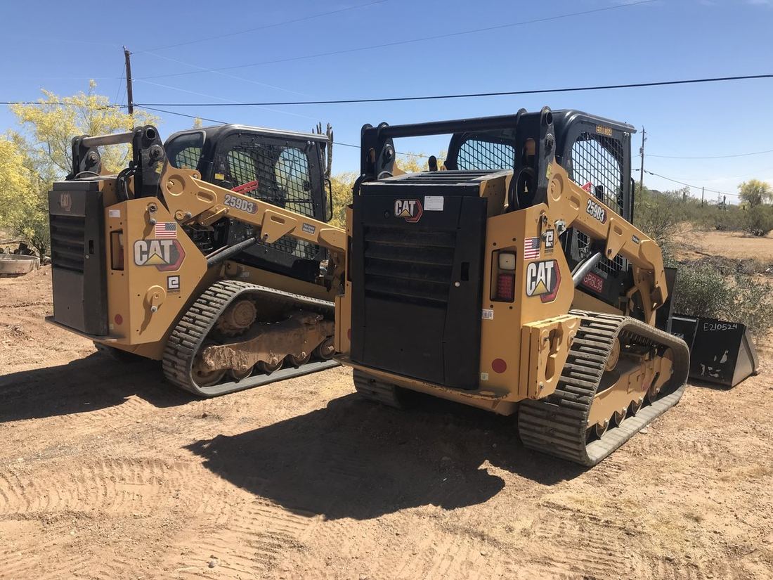 Two matched CAT skid steers parked in the desert
