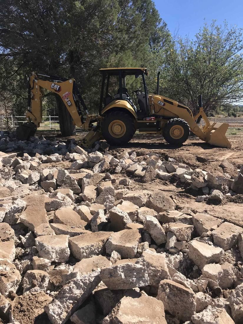 Pile of broken concrete demolition debris staged next to a CAT 416F backhoe on a rural Arizona property