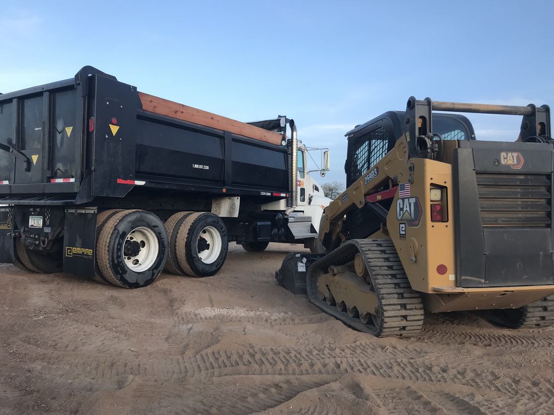 Dump truck and CAT skid steer staged on a Mesa job site